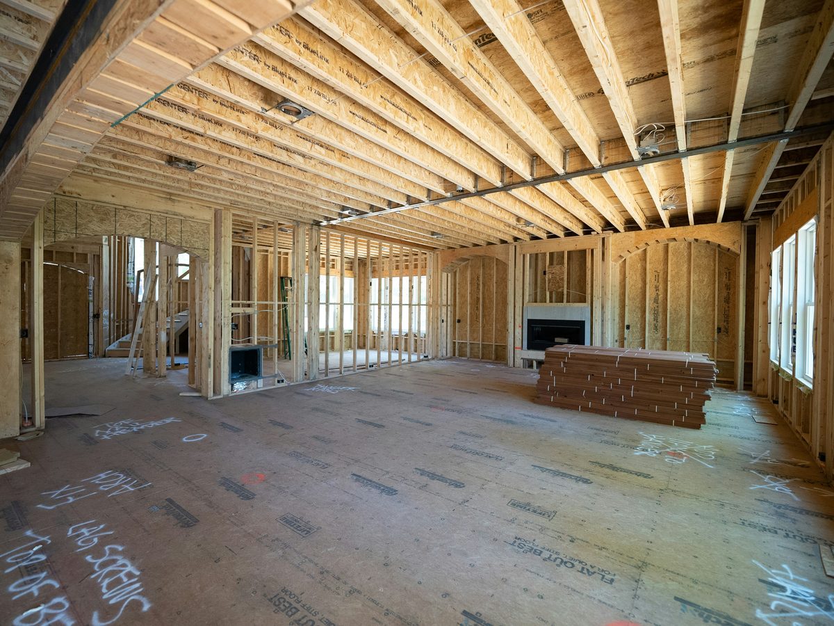 Interior of new construction home mid-framing with subfloor, lumber stacks, and exposed studs