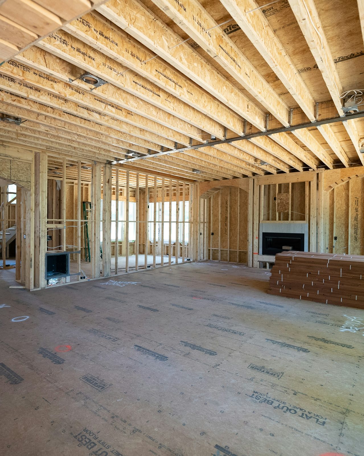 Interior of new construction home mid-framing with subfloor, lumber stacks, and exposed studs