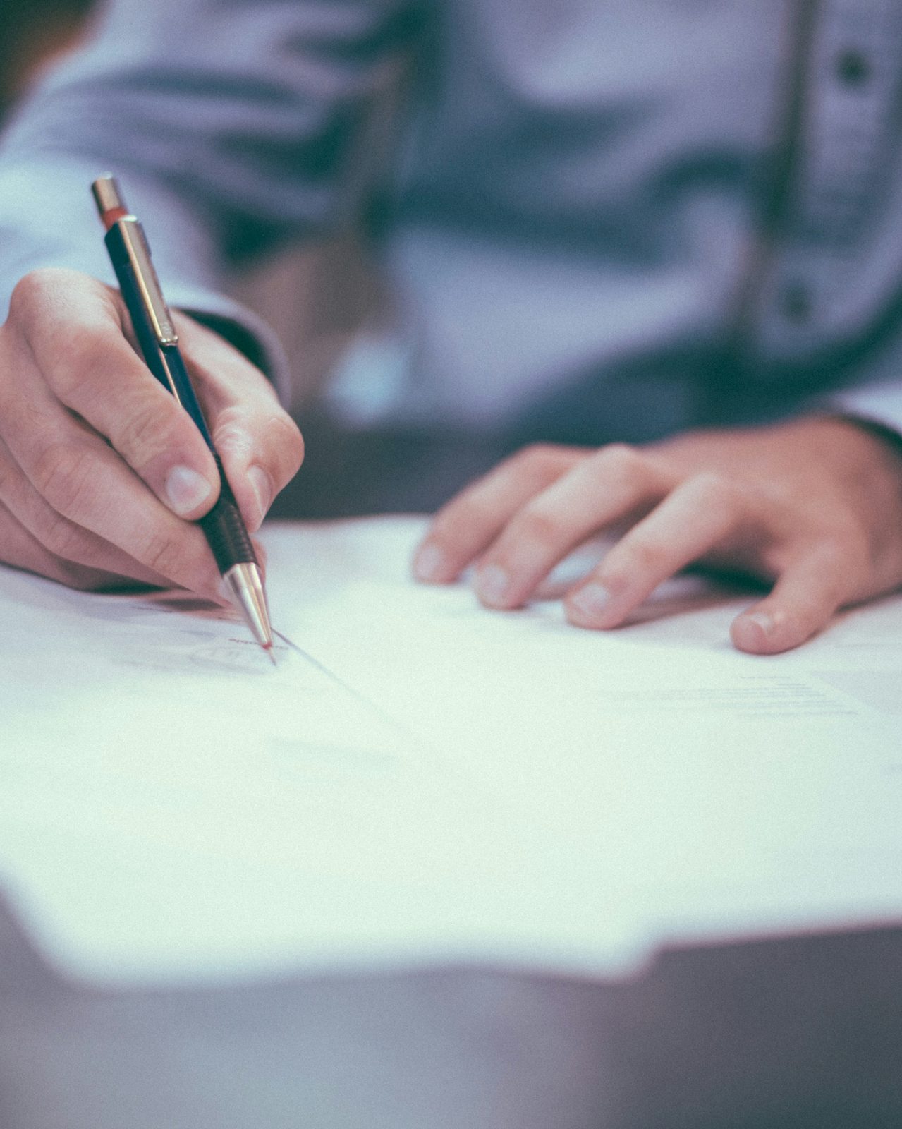 Investor signing offer paperwork at desk with pen in hand